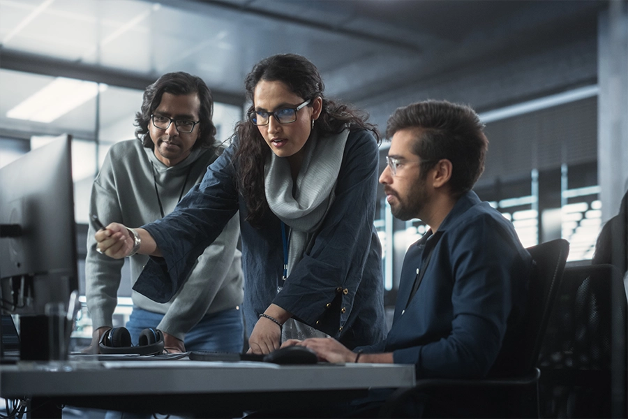South Asian team in office, two men look at computer screen as a woman points to it 